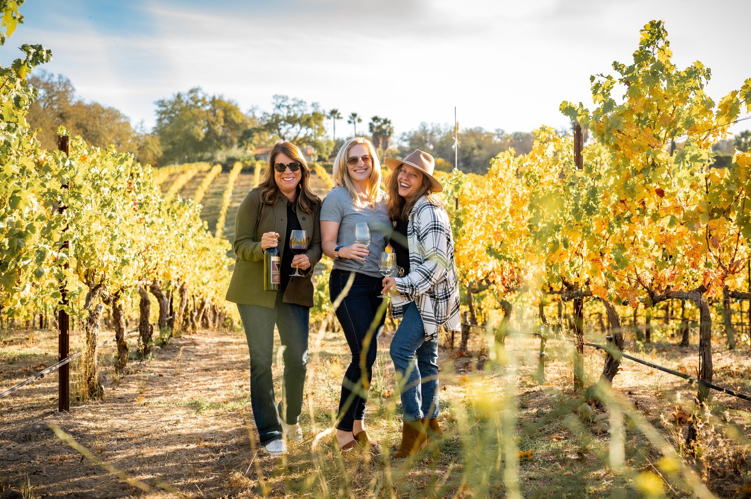 women in a vineyard drinking wine out of glasses